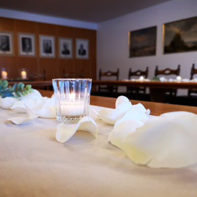 Bild vergrößern: Blick in den Sitzungssaal, im Vordergrund eine kleine Kerze im Glas umringt von weißen Rosenblättern